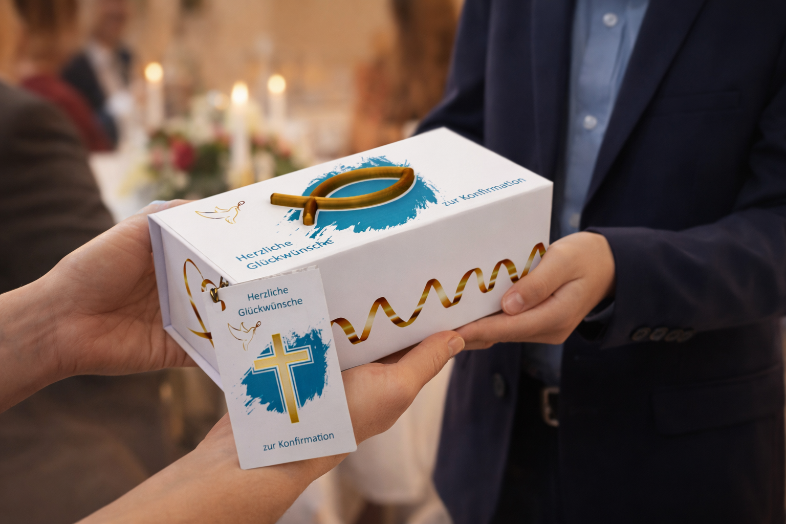Eine Person in festlicher Kleidung überreicht eine längliche weiße Geschenkbox zur Konfirmation an eine andere Person. Die Box ist mit einem goldenen 3D-Fischsymbol auf türkisfarbenem Hintergrund und einer goldenen Wellenlinie verziert. An der Seite hängt eine Grußkarte mit Kreuzmotiv und dem Text ‚Herzliche Glückwünsche zur Konfirmation‘. Der Hintergrund ist warm und unscharf und erinnert an eine Feier.