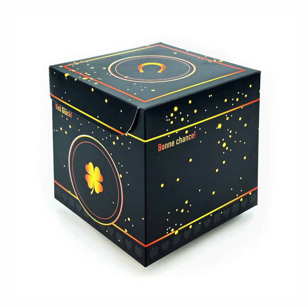 Geschlossene Rätselbox Glück in Schwarz mit goldenen Sprenkeln und Kleeblatt-Motiv (Viel Glück) auf der Seite und Hufeisen auf dem Deckel auf weißem Hintergrund.