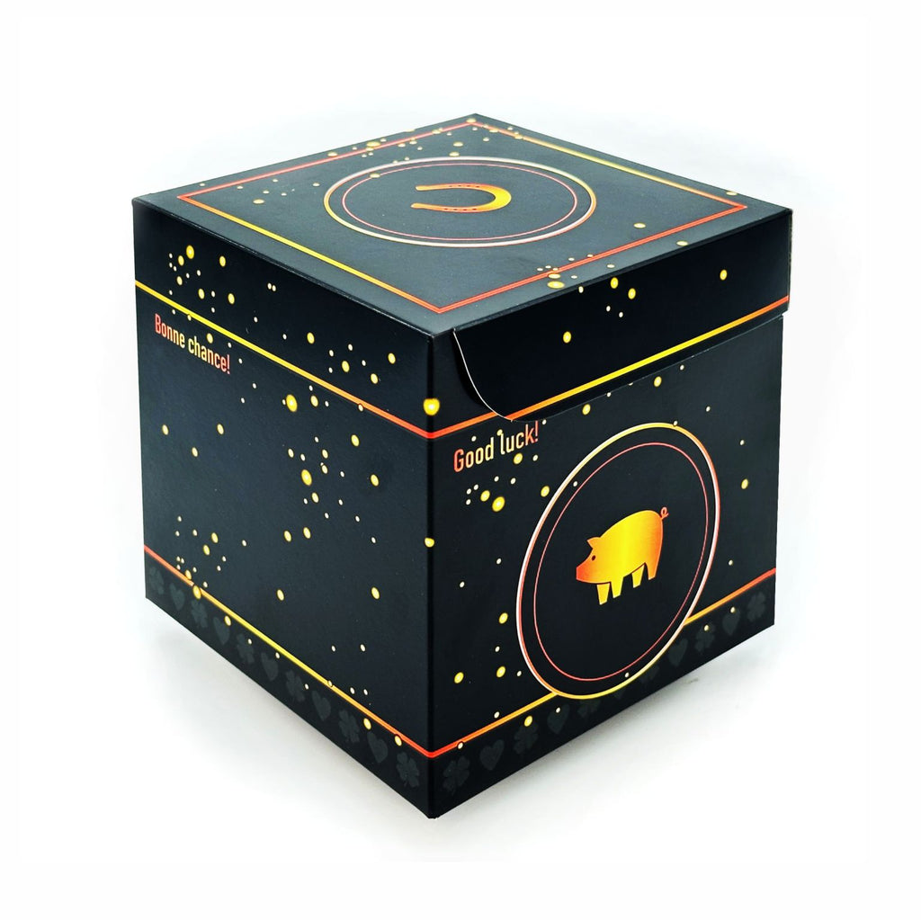 Geschlossene Rätselbox Glück in Schwarz mit goldenen Sprenkeln, Glücksschwein-Motiv auf der Seite (Good luck!) und Hufeisen auf dem Deckel auf weißem Hintergrund.