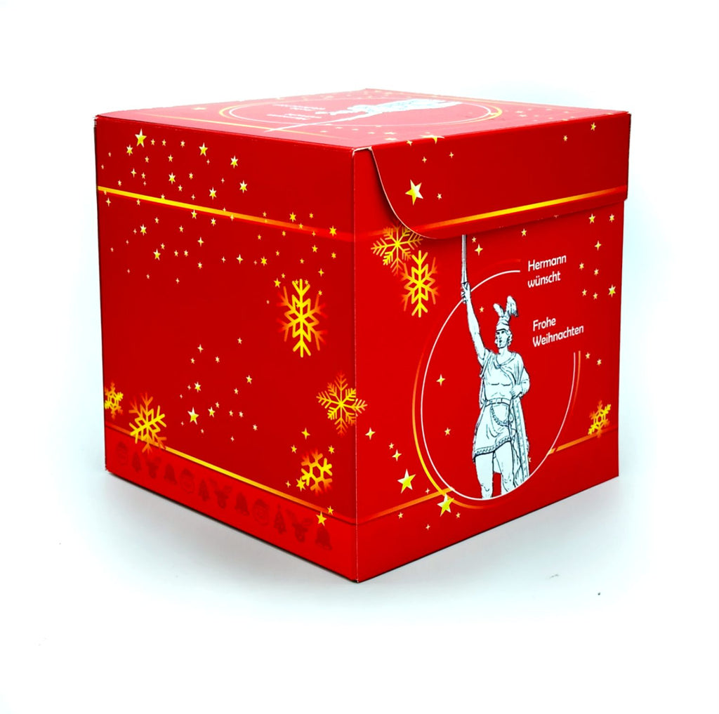 Rätselbox Weihnachten Hermannsdenkmal in Rot mit goldenen Stern- und Schneeflockenmotiven sowie Hermannsdenkmal-Illustration auf der Seite. Text: Hermann wünscht Frohe Weihnachten