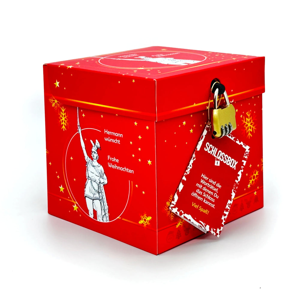 Geschlossene Rätselbox Weihnachten Hermannsdenkmal in Rot mit goldenen Stern- und Schneeflockenmotiven, goldenem Zahlenschloss und rotem Rätselheft-Anhänger. Text: Hermann wünscht Frohe Weihnachten