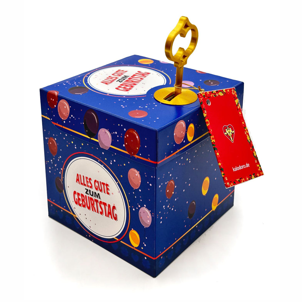 Blaue Schlossbox zum Geburtstag mit Ballonmuster und rundem Schriftzug ‚Alles Gute zum Geburtstag‘, dekorativer goldener Schlüssel steckt oben in der Box, rote Geschenkanhängerkarte seitlich befestigt, auf weißem Hintergrund.