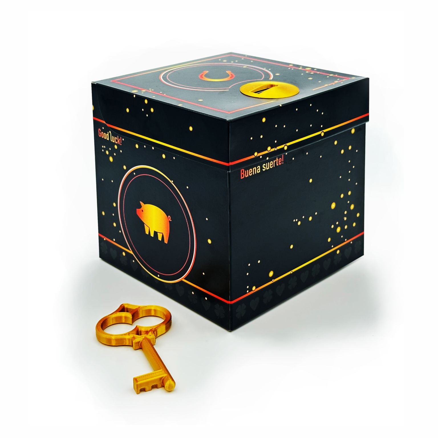 Geschlossene Schlossbox Glück in Schwarz mit goldenen Sprenkeln und Glücksschwein-Motiv, seitlich Schriftzüge ‚Good luck‘ und ‚Buena suerte‘, goldener Schlüssel liegt vor der Box.